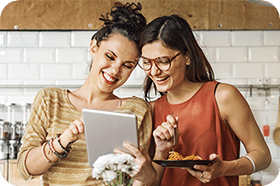 Two female friends happy in the kitchen using a tablet