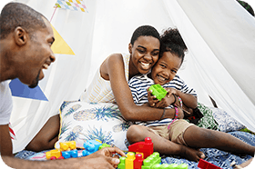 Father and mother playing their child outside under a tent with toys