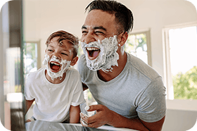 Father and son smiling in the mirror with shaving cream on their faces