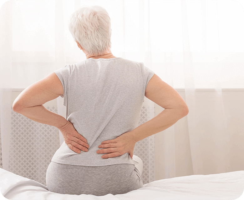 Senior woman getting out of bed holding lower back in pain