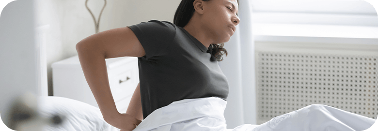 Young woman getting out of bed with lower back pain