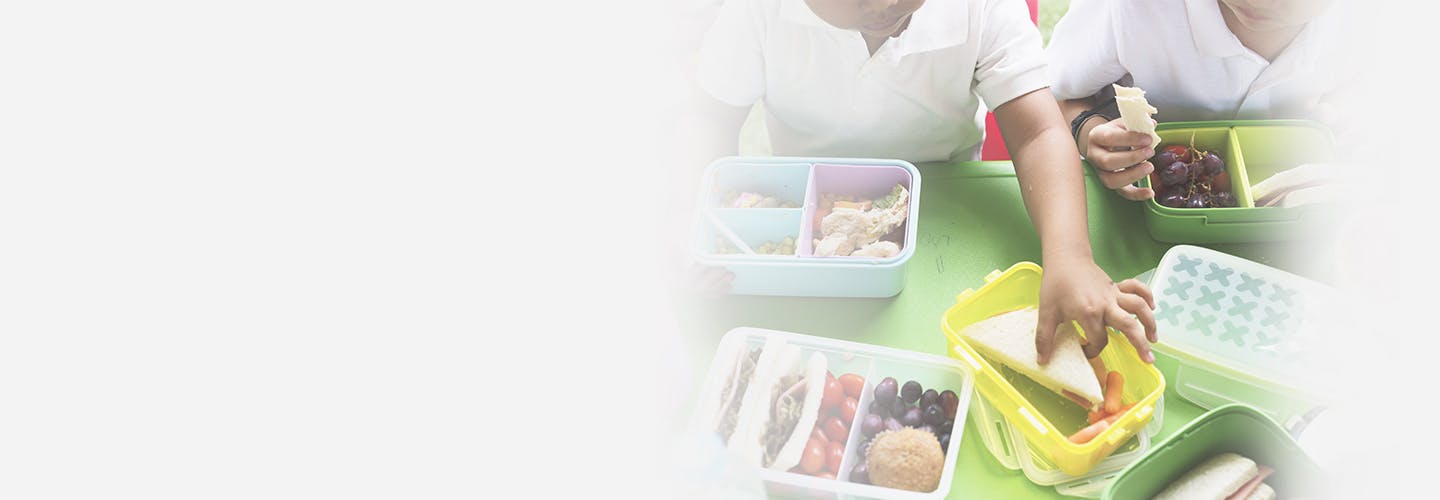 Group of kindergarten students eating lunch from lunchboxes