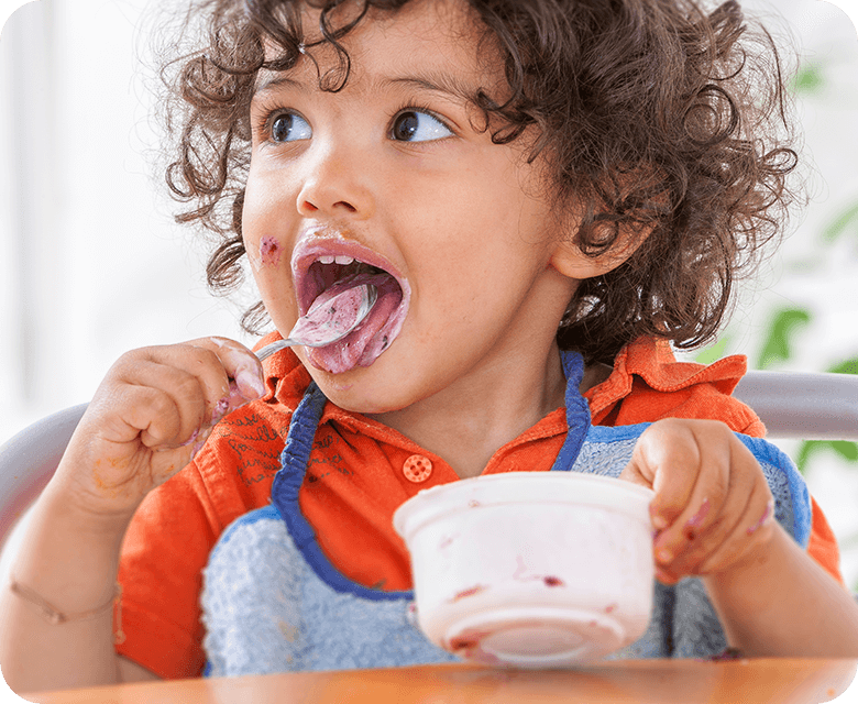 Toddler sitting in a high chair eating greek yoghurt