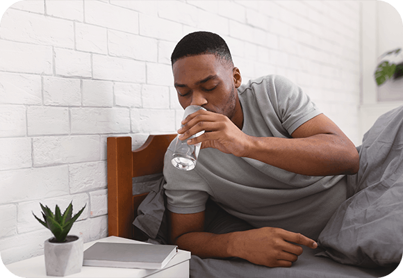 Man in bed drinking a glass of a water