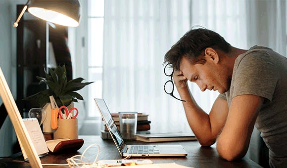 Man sitting at desk stressed staring down at laptop
