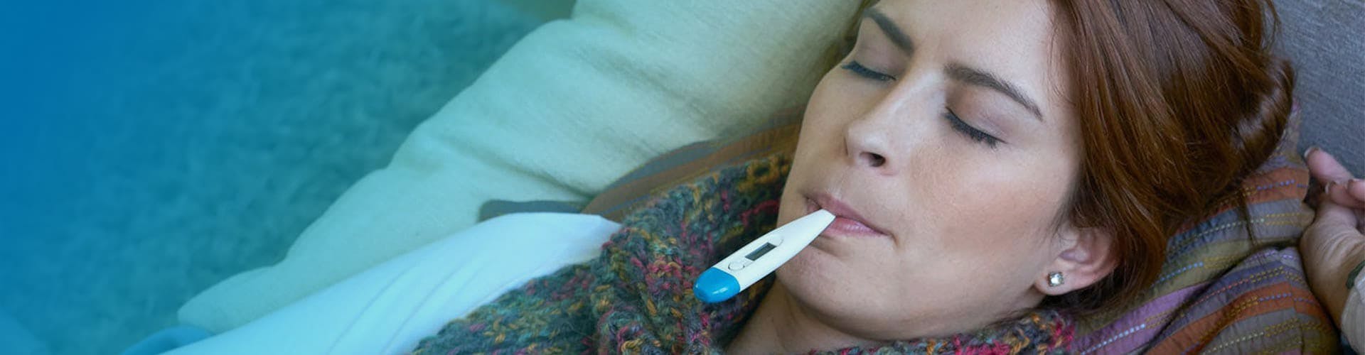 Young woman taking her temperature by using a digital thermometer. 