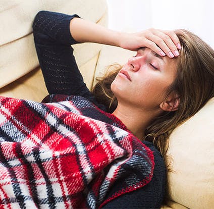 Woman lying down trying to determine her body temperature by putting her hand in her forehead. 