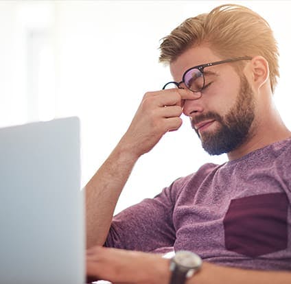 Man in front of a laptop with a headache. 