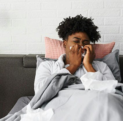 Woman lying on her bed with nasal congestion, blowing her nose. 