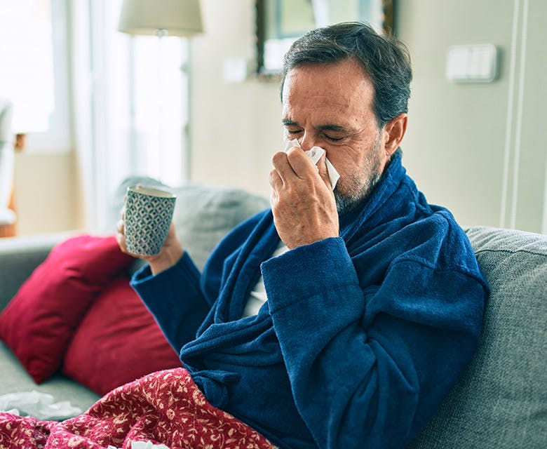 Middle aged man with flu sitting on the couch holding a mug