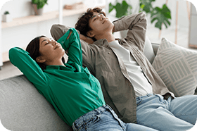 Peaceful young Asian couple relaxing on sofa with their hands behind heads