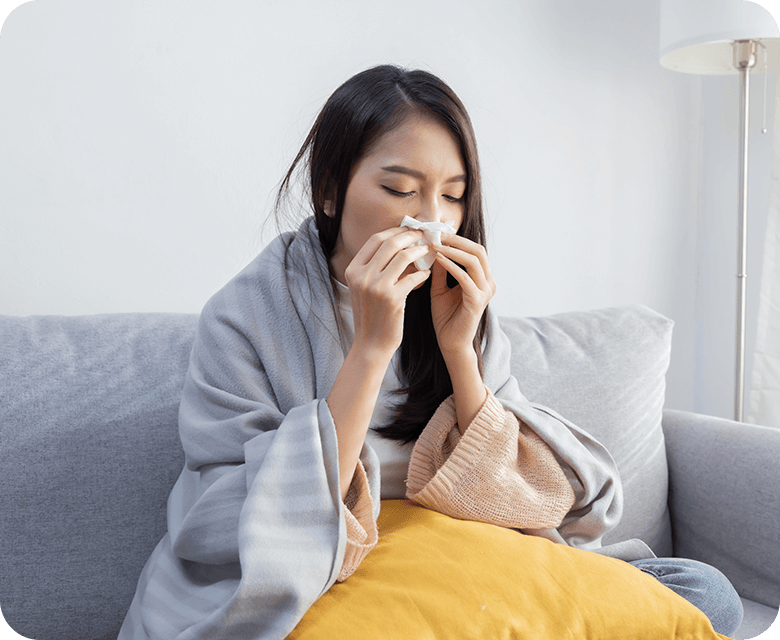 young sick asian woman blowing nose while sitting on the sofa