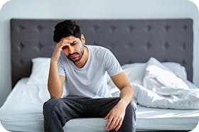Man Sitting On His Bed With A Headache