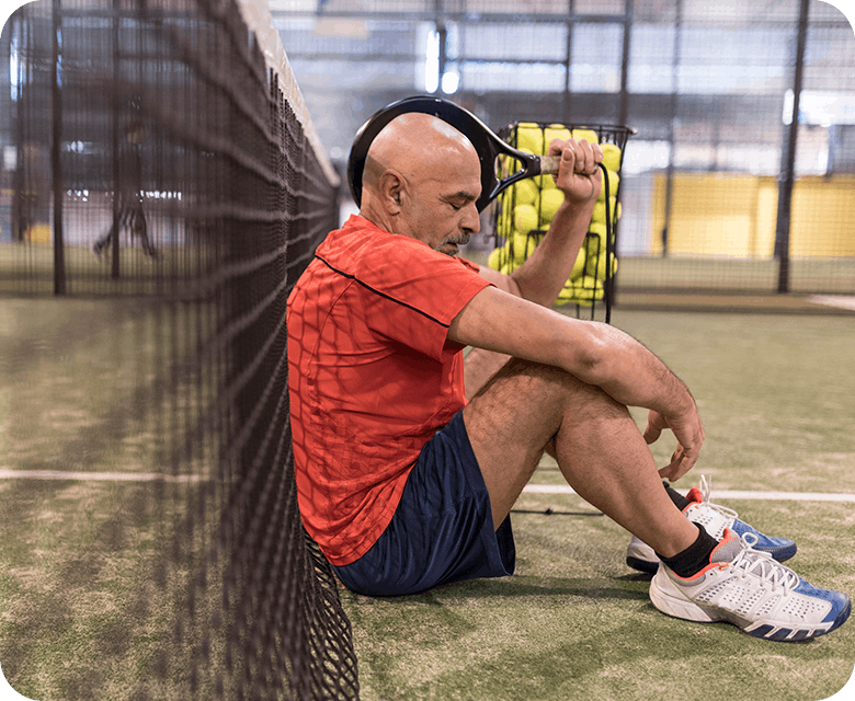 Man Sitting In Tennis Court Suffering From A Headache 