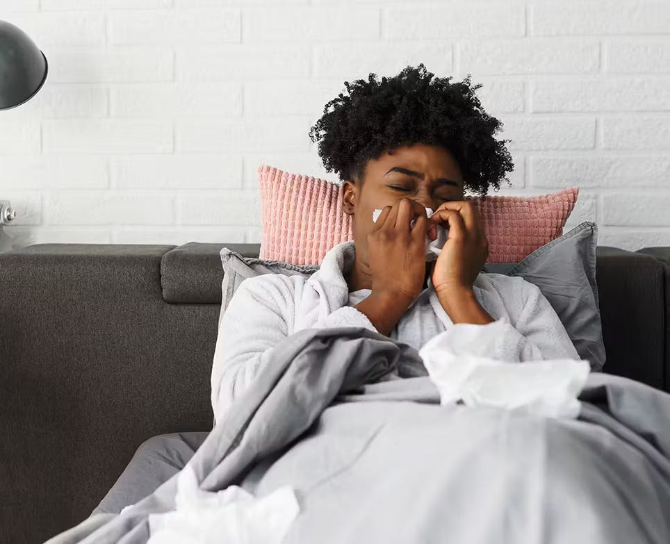 Mujer recostada en su cama con congestión nasal, limpiando su nariz.