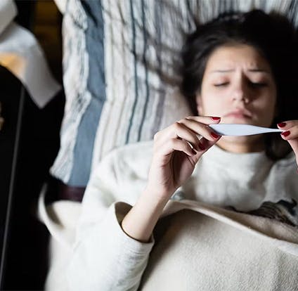 Adulta mayor con congestión nasal, limpiando su nariz y tomando una bebida caliente. 