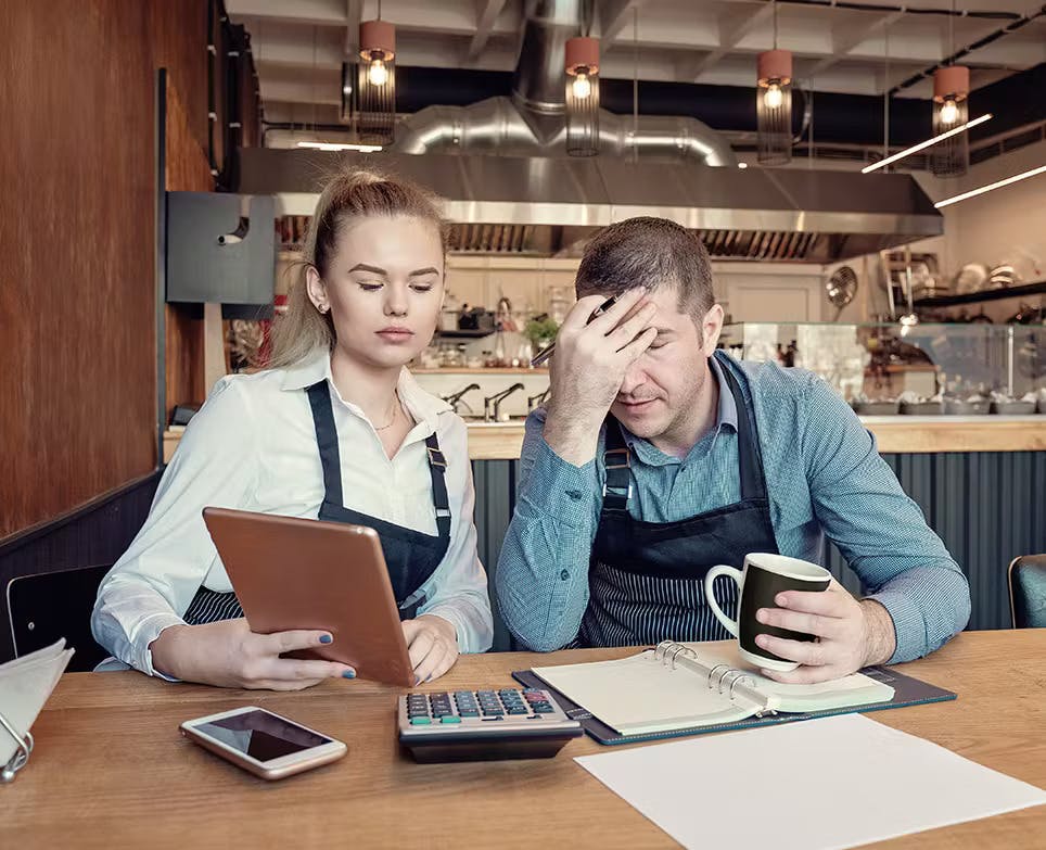 Pareja trabajando. El hombre se agarra la cabeza en señal de dolor.