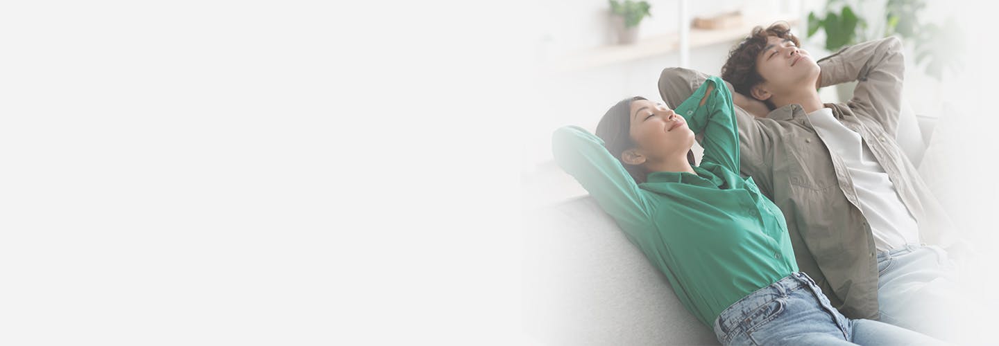 Peaceful young Asian couple relaxing on sofa with their hands behind heads