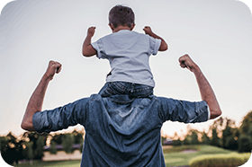 Son sitting on father's shoulders having fun outdoors