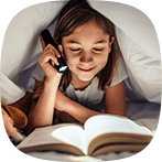 Flicka läser bok under täcke med ficklampa