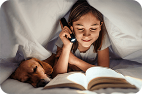 Flicka läser bok med ficklampa