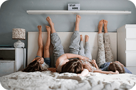 Mamma och döttrar ligger i säng med ben mot vägg