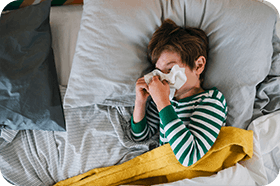 Förkyld pojke i randig tröja snyter sig i sängen
