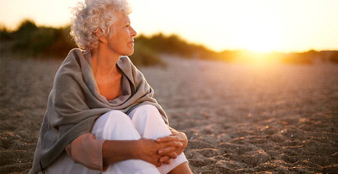 Kvinde sidder sammenbøjet på stranden ved solnedgang 