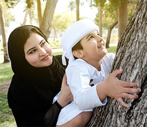 A mother holding her son as he climbs a tree