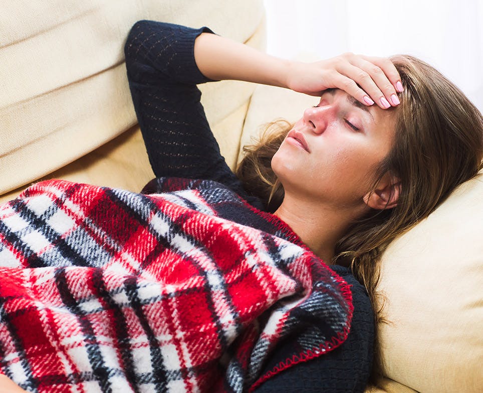 Woman lying down trying to determine her body temperature by putting her hand in her forehead. 