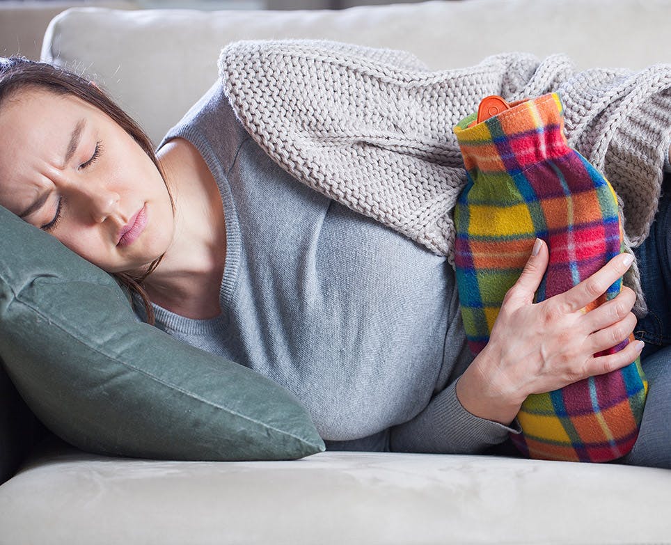 Woman holding a hot water bag against her abdomen. 