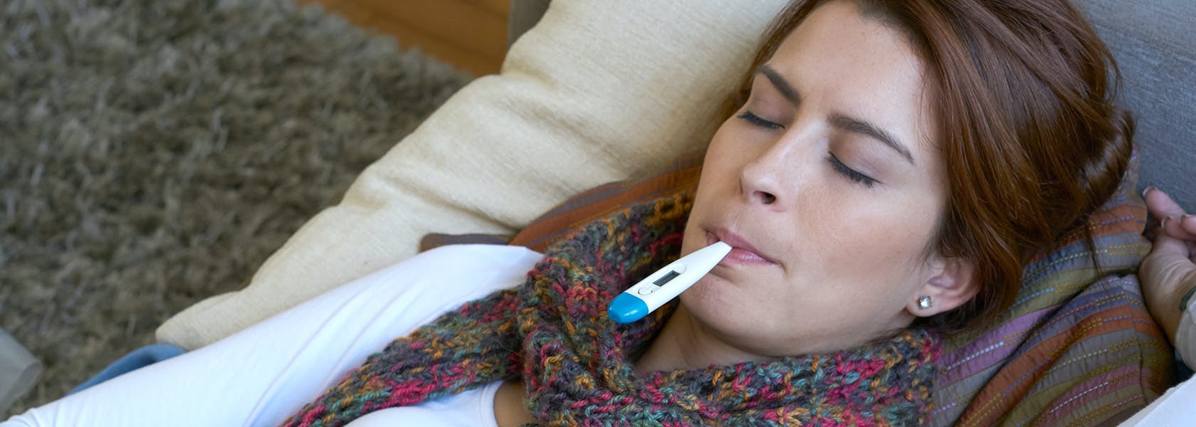 Young woman taking her temperature by using a digital thermometer. 