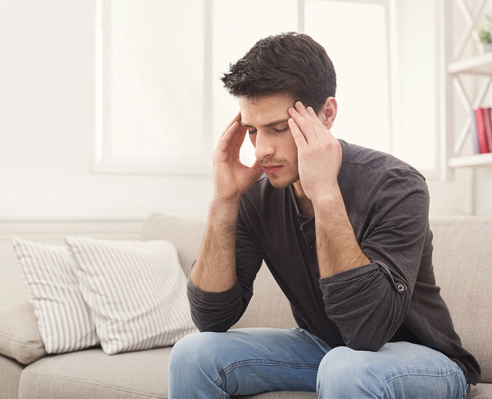 Young man grabbing his aching head from the sides. 