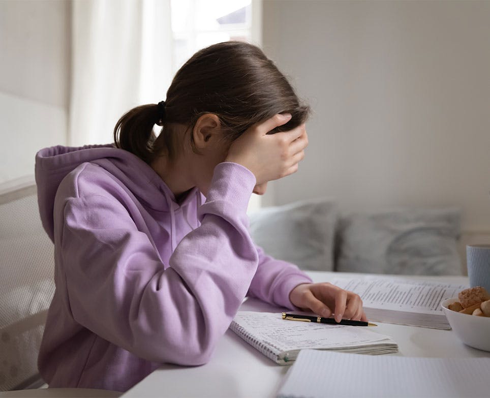 Girl trying to study while holding her aching head. 