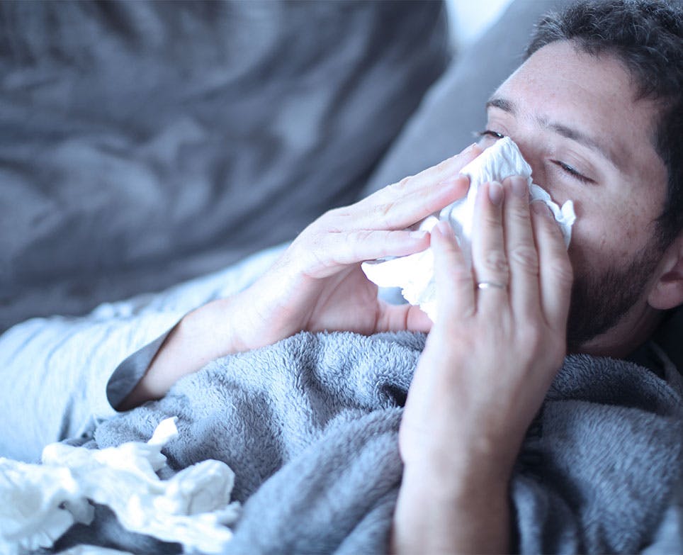 Man with nasal congestion blowing his nose, lying on his bed. Man with nasal congestion blowing his nose, lying on his bed.