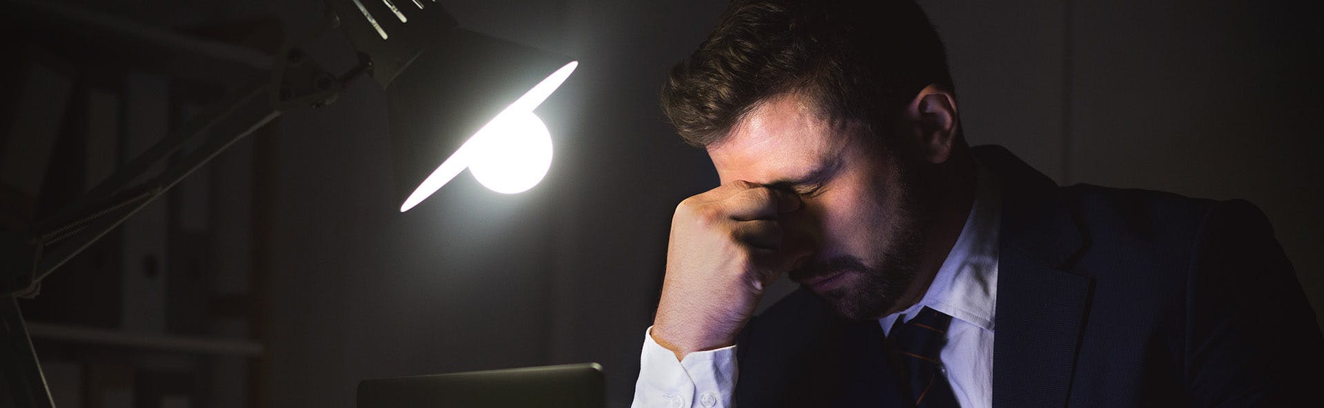 Man in the gloom, grabbing his nose because of a strong headache. 