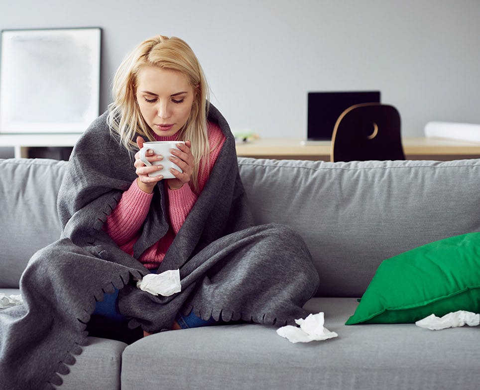 Woman with flu symptoms having a hot drink. 