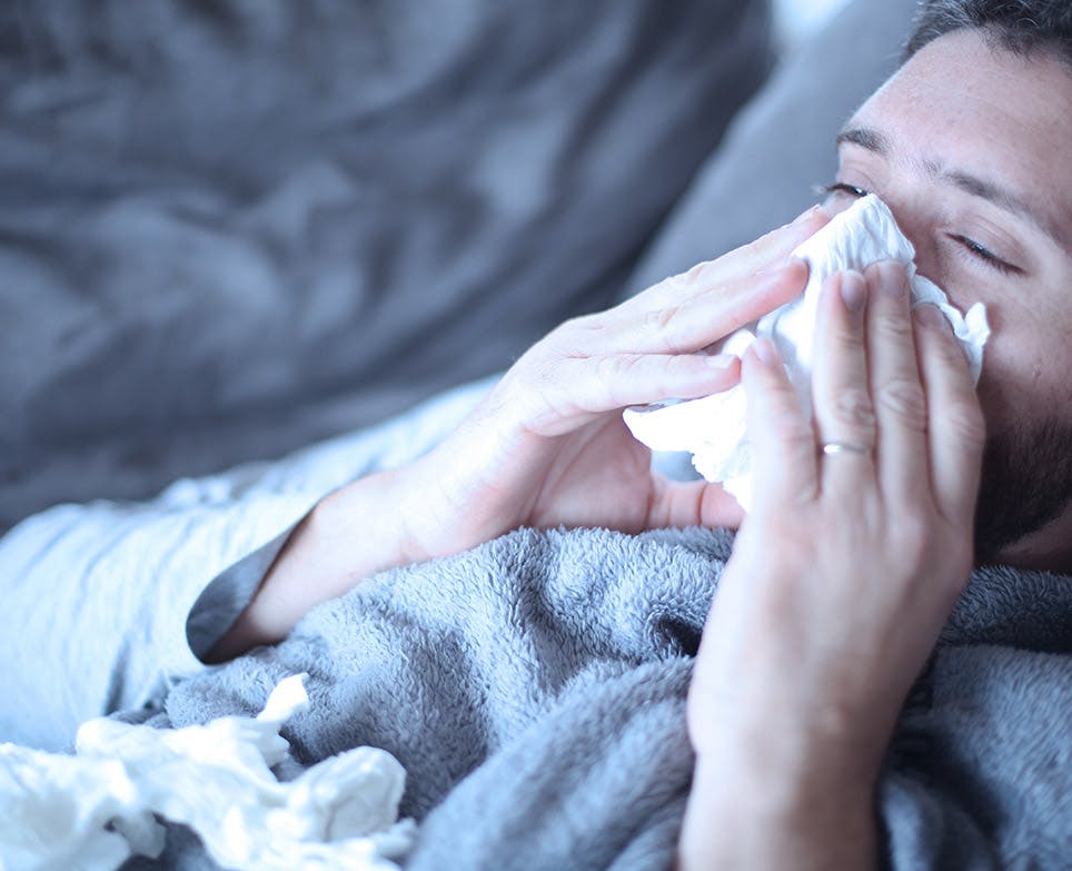 Man with nasal congestion blowing his nose, lying on his bed. 