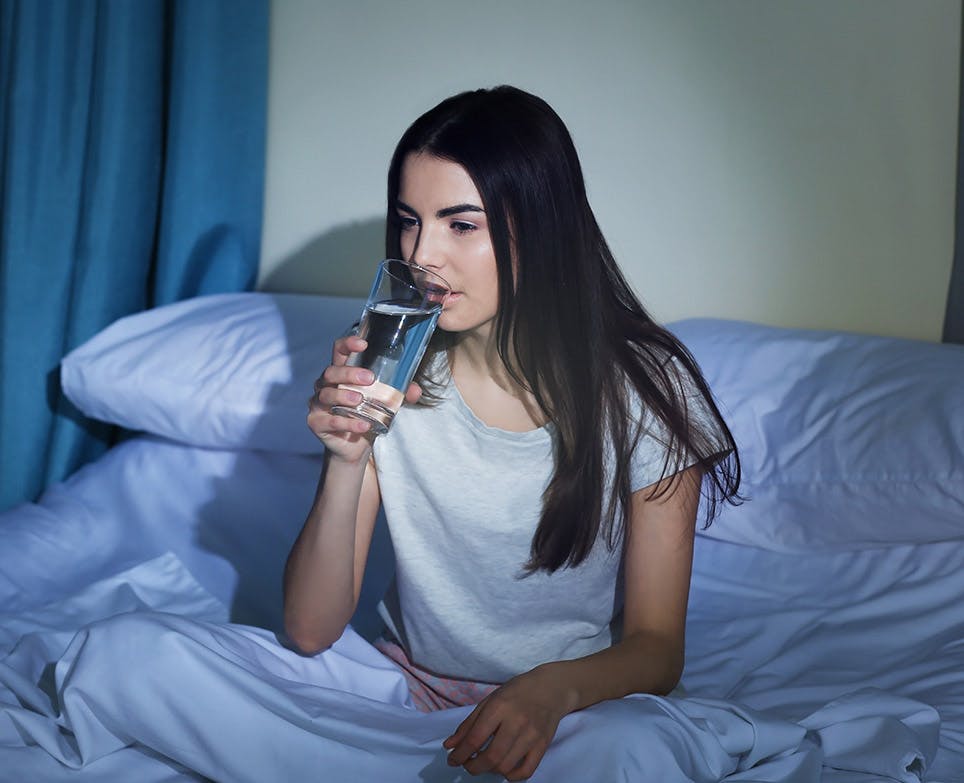Young woman drinking a glass of water in her bed. 