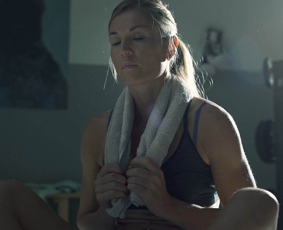 Woman with her eyes closed holding a towel around her neck, due to exhaustion after an exercise session. 