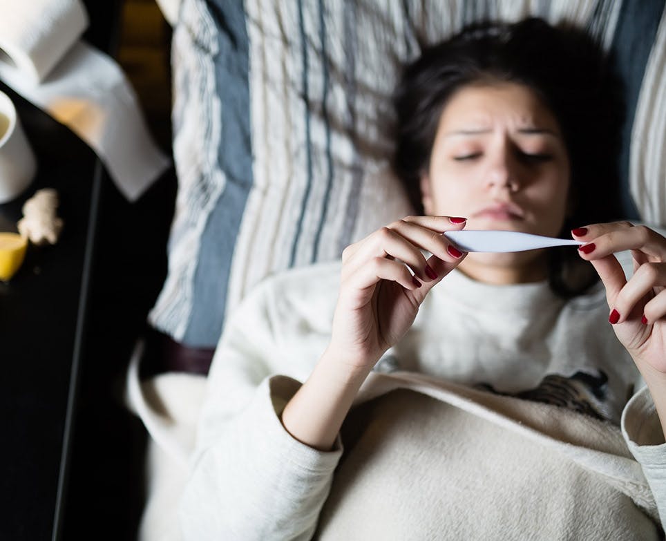 Woman taking her temperature on digital thermometer. 