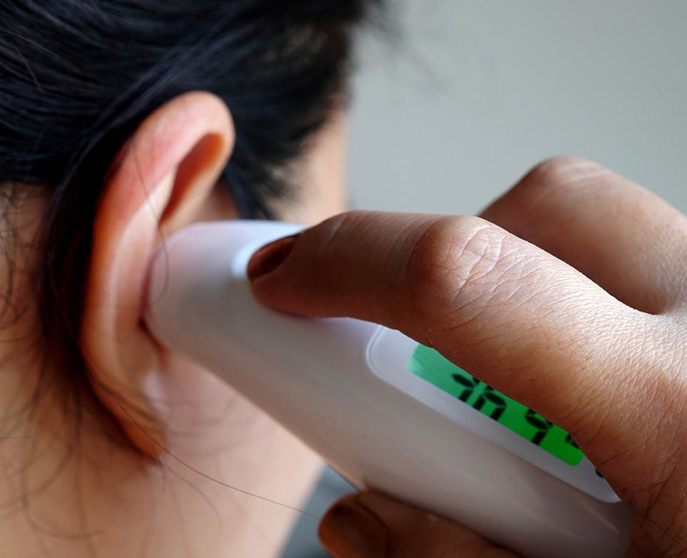 Person taking their temperature with a digital ear thermometer. 