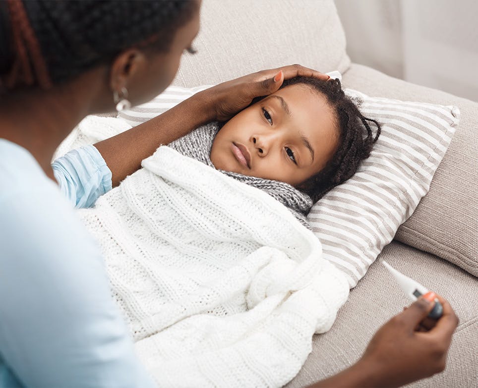 Mother touching her daughter's foread while taking her temperature with a digital thermometer. 