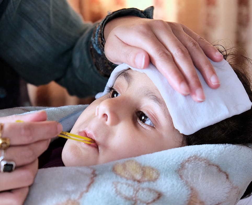 A sick child laying down while his mother takes his temperature with a traditional thermometer. 