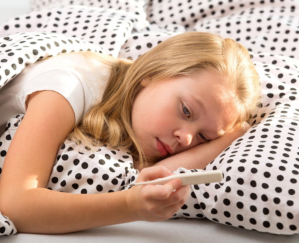 Little girl reading her temperature on a digital thermometer. 