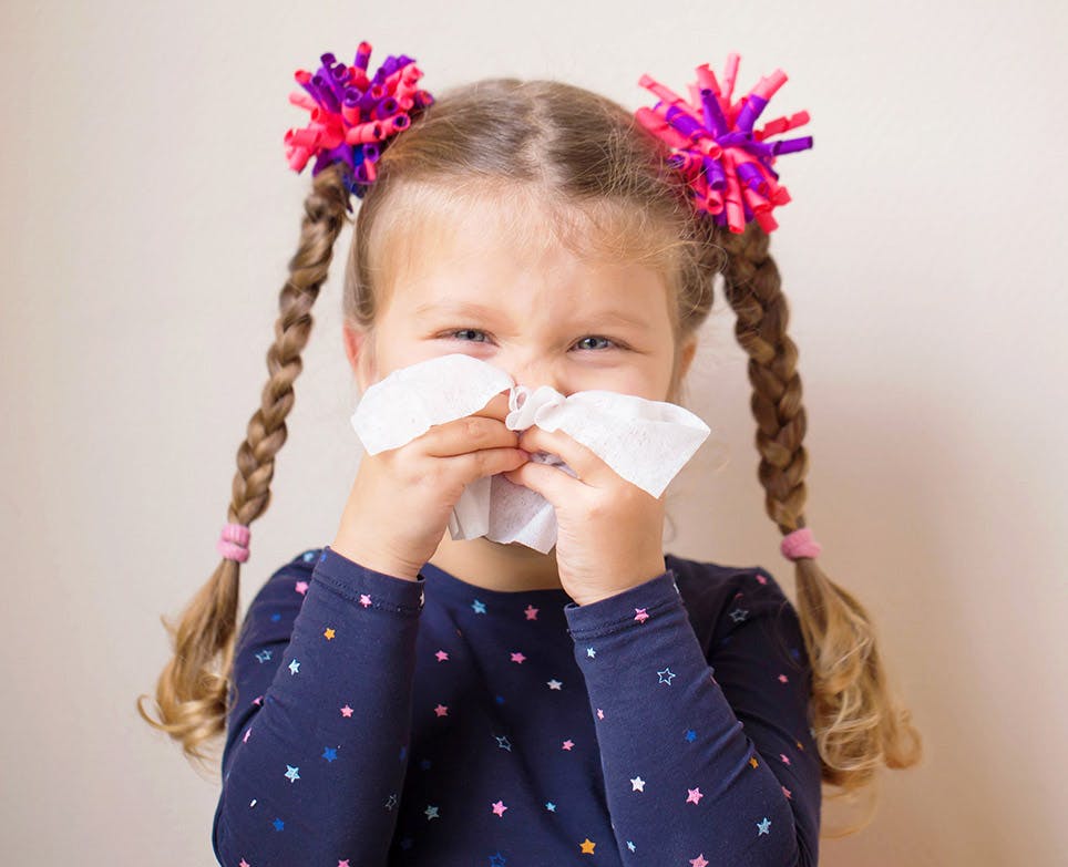 Little girl blowing his nose with a tissue. 