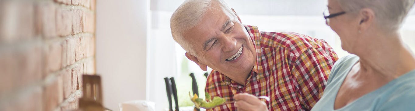 Pareja mayor comiendo ensalada y sonriendo. 