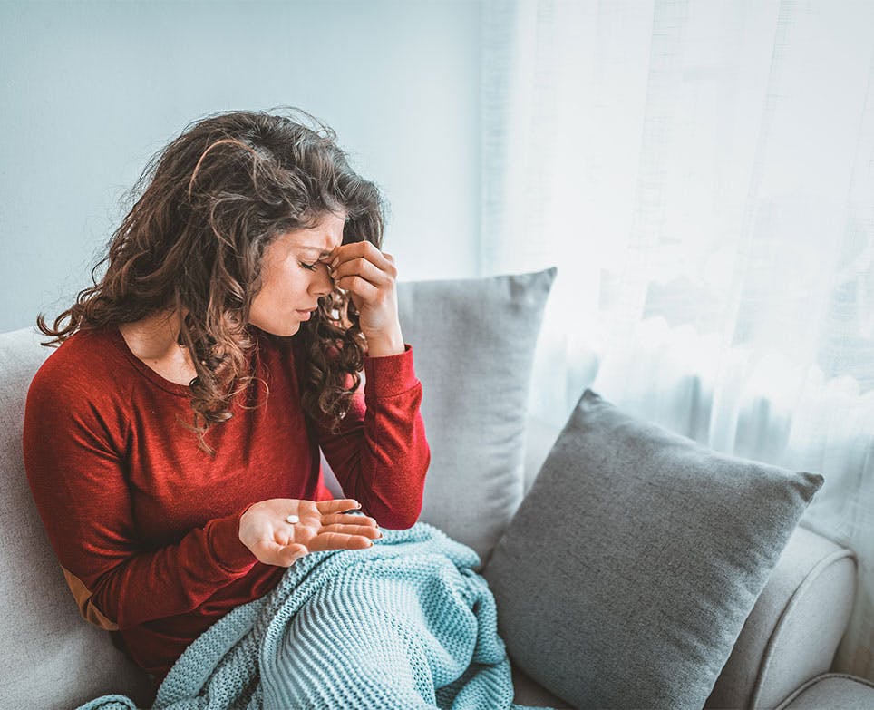 Mujer se prepara para tomar una píldora y se toca la parte superior de la nariz en señal de dolor. 