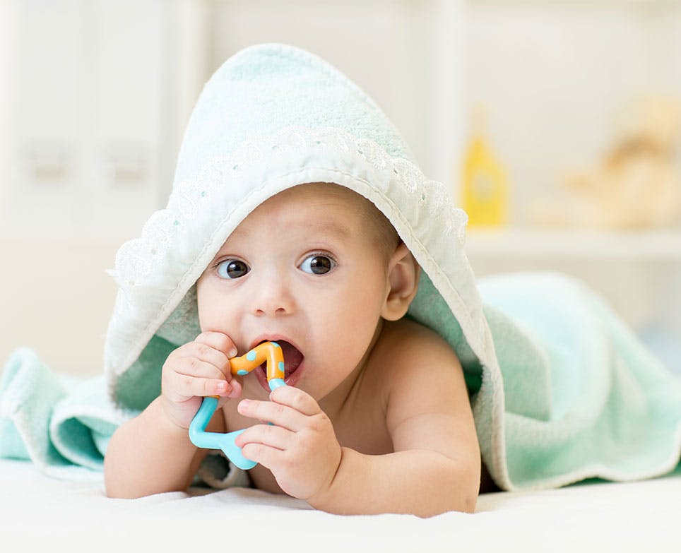 Bebé mordiando un juguete para dentición después de un baño. 