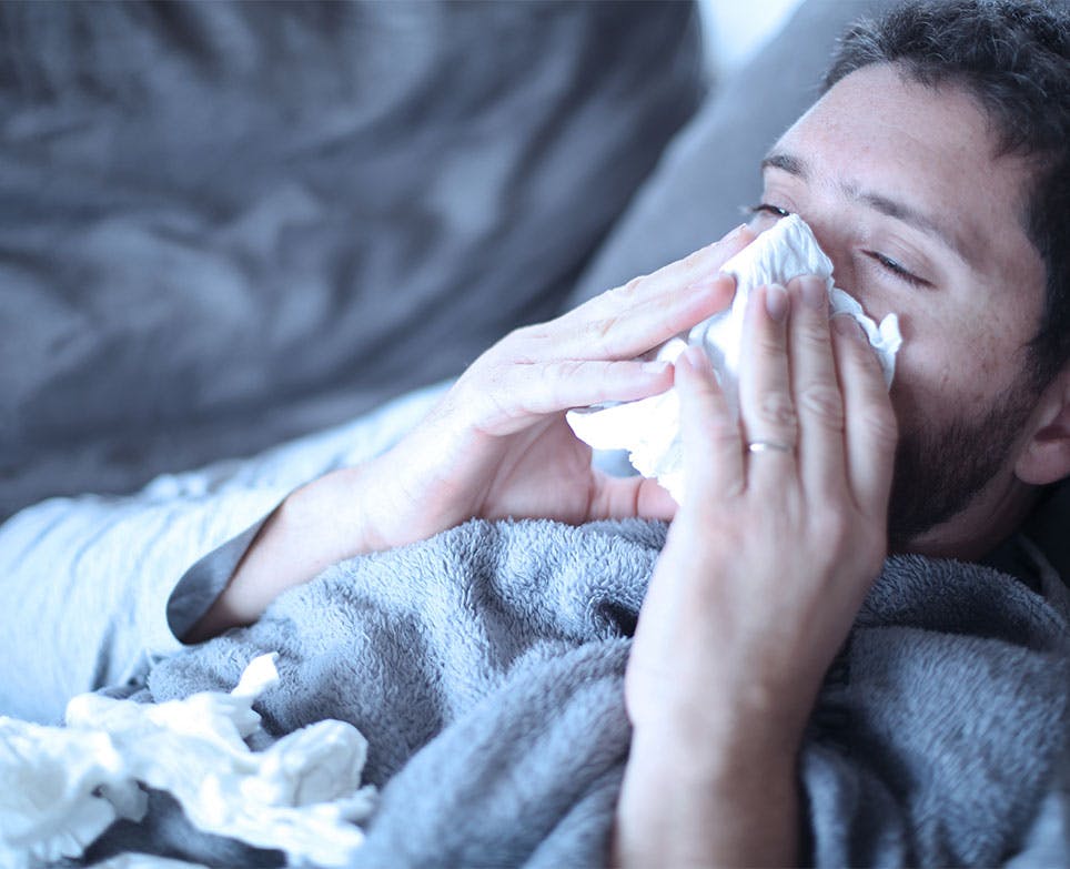 Hombre con congestión nasal limpiando su nariz, recostado en una cama. 